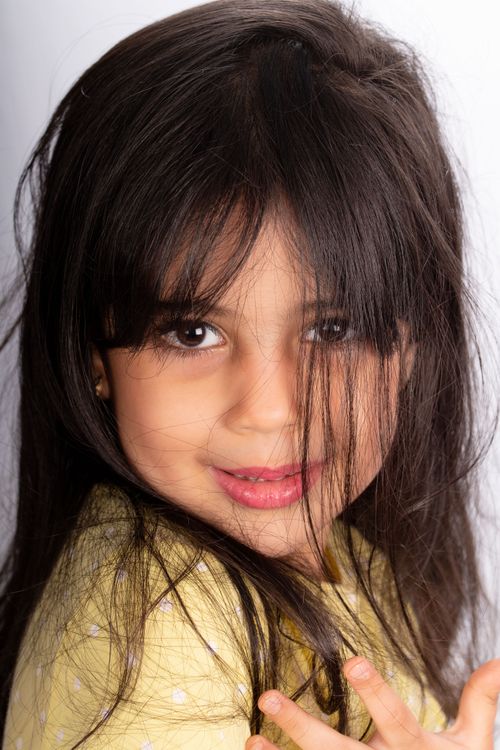 Free Adorable young girl with long hair smiling brightly in a studio portrait. Stock Photo