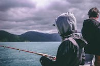 两人在海边多云的天空下钓鱼，欣赏山景