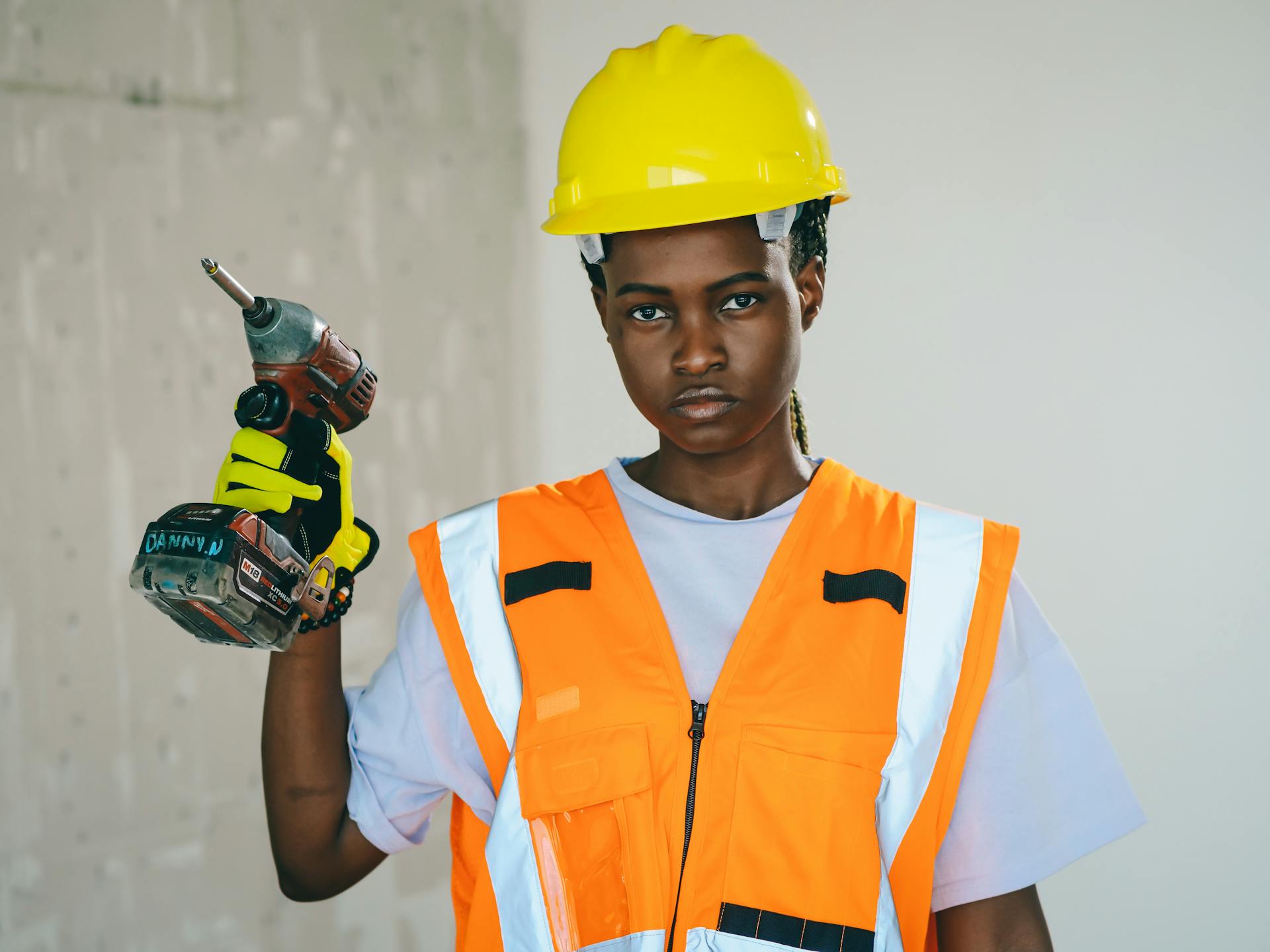 A determined construction worker holding a drill in safety gear indoors.