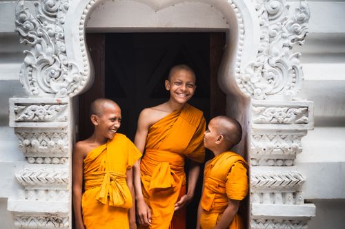 Free Three young Buddhist monks in saffron robes smiling in a decorative doorway in India. Stock Photo