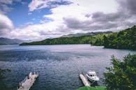 在多云的天空下，宁静的湖景中有码头、船只和郁郁葱葱的绿地