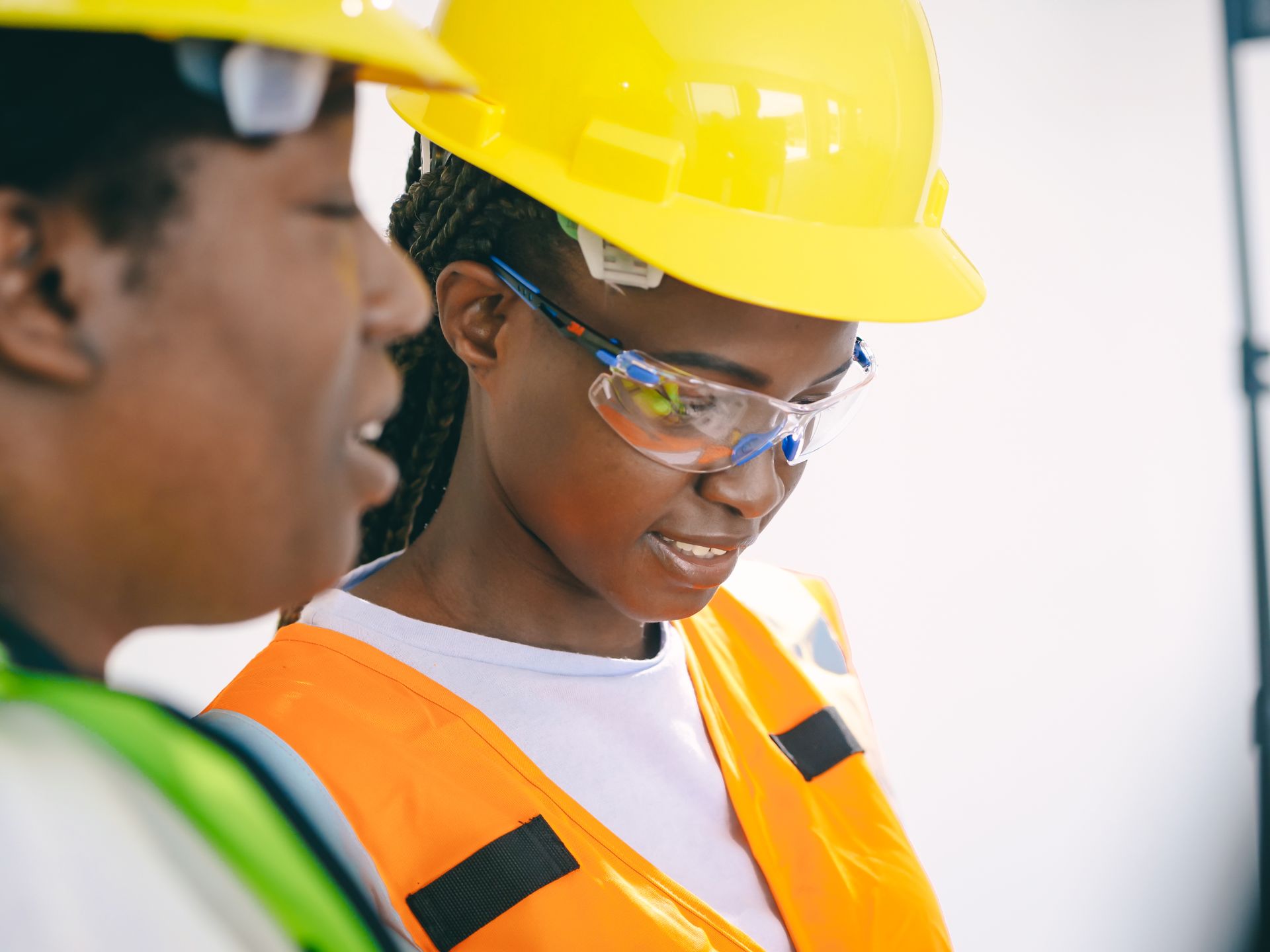 Two women engineers on site with hard hats and safety vests focusing on a task.