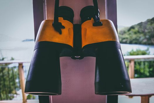 Close-up of yellow binoculars hanging inside, overlooking a scenic outdoor view.