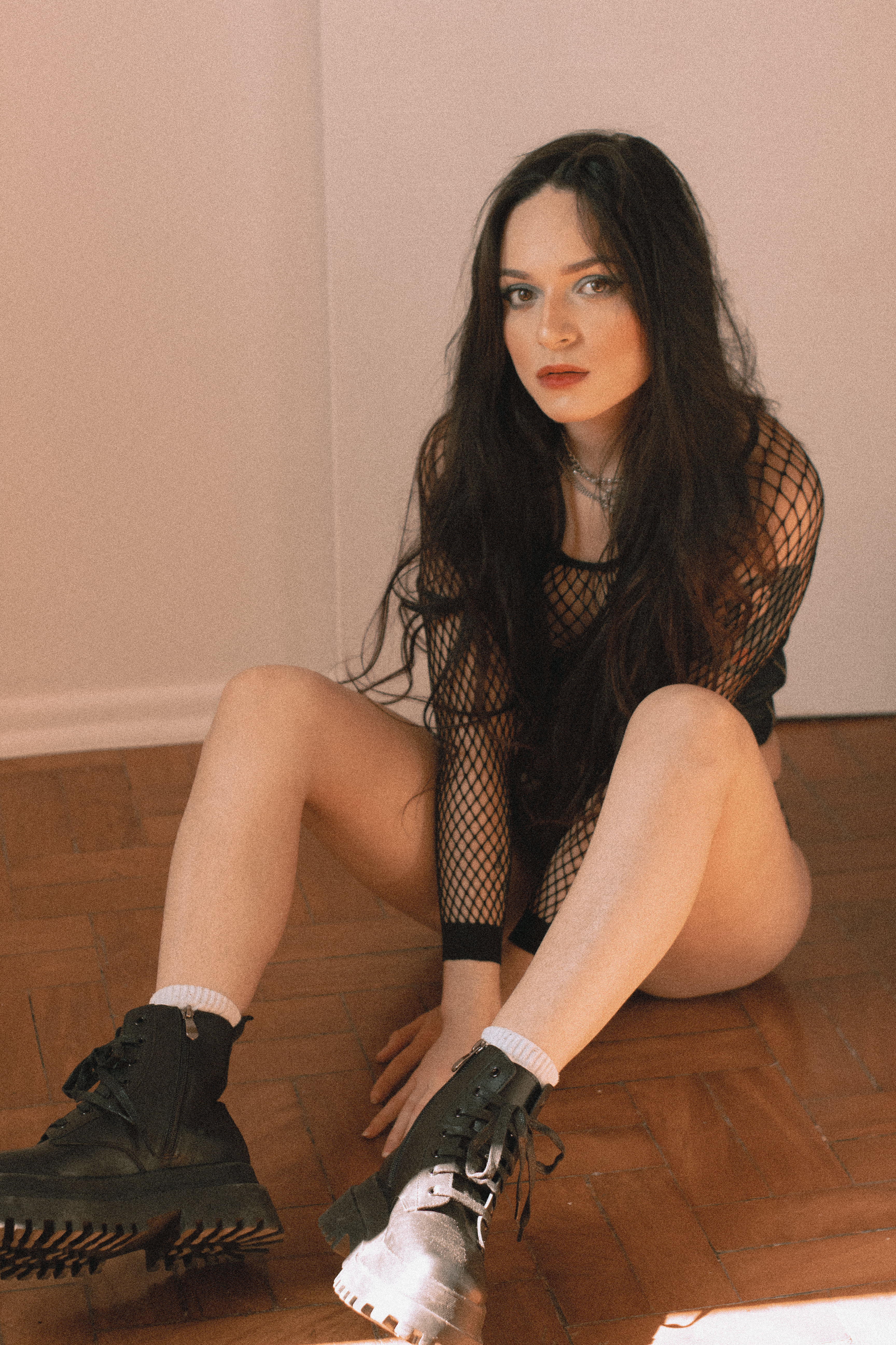 Stylish young woman wearing a fishnet top, sitting on a wooden floor in Santo André.