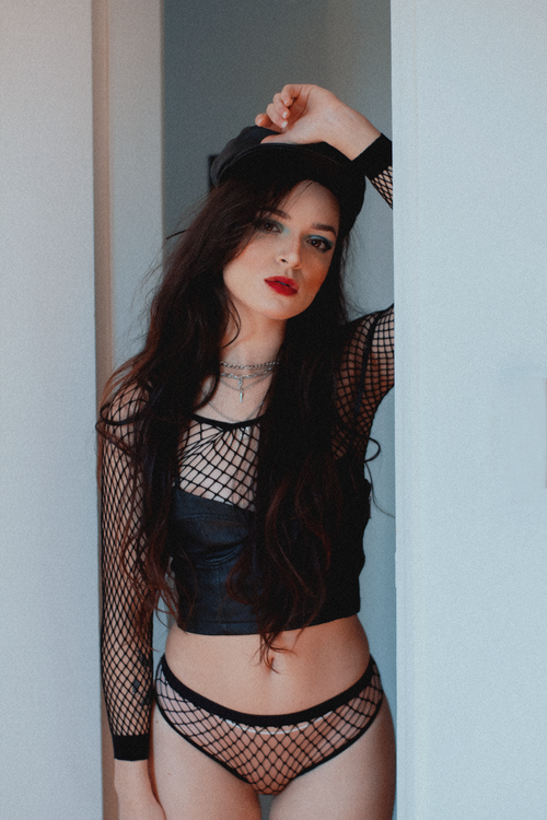 Free Fashionable woman posing in fishnet outfit, leaning casually on a doorframe, exuding confidence. Stock Photo