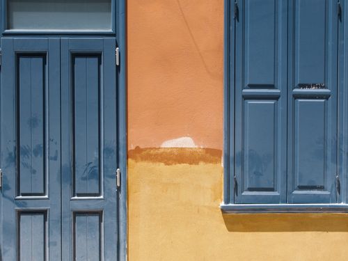 Free Vibrant orange wall with a blue door and window in daylight, showcasing contrasting colors. Stock Photo