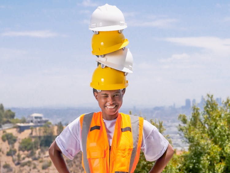 Smiling Woman With Stacked Hardhats On Her Head 