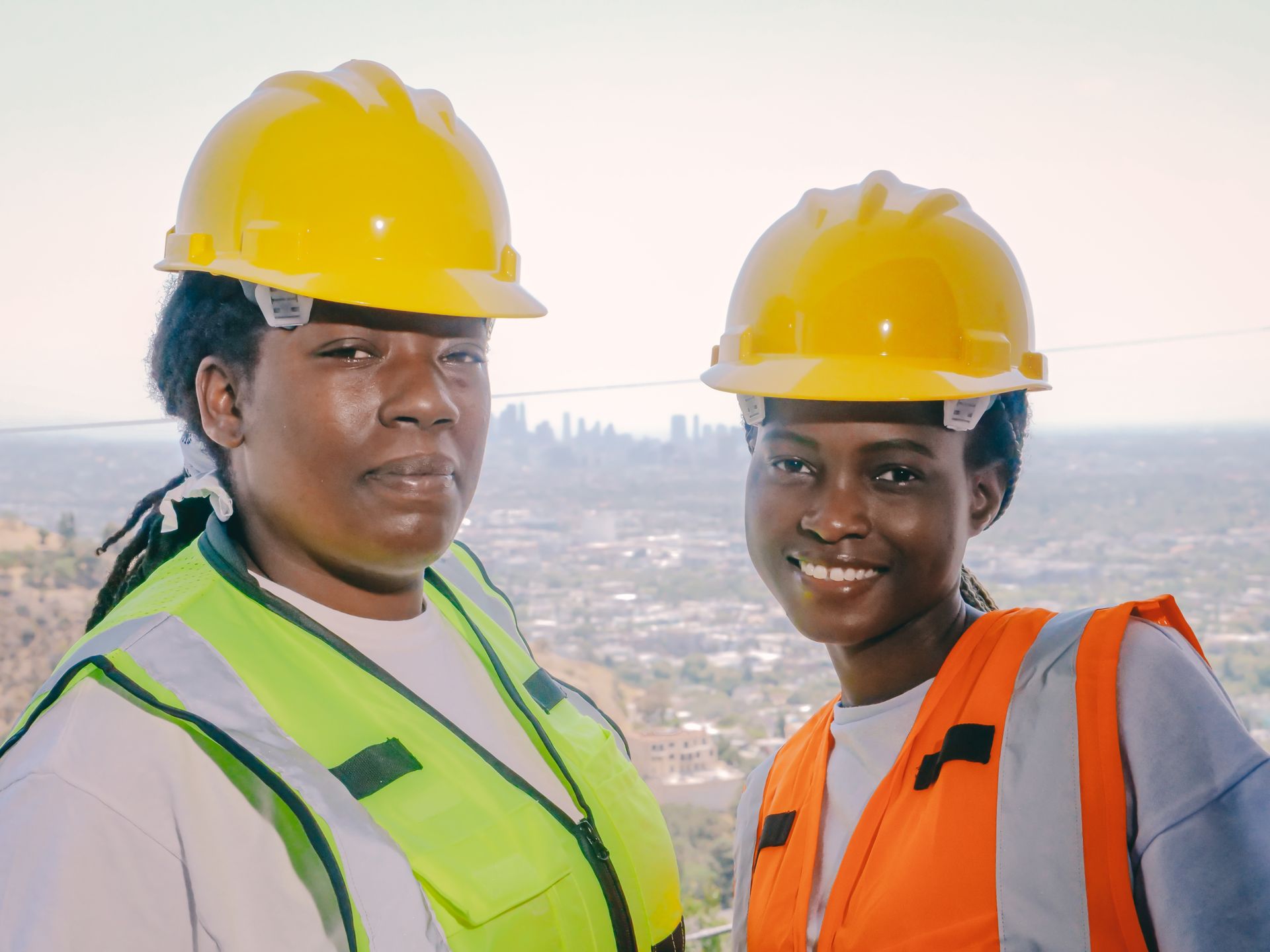 Two female construction workers wearing helmets and safety vests at a job site.