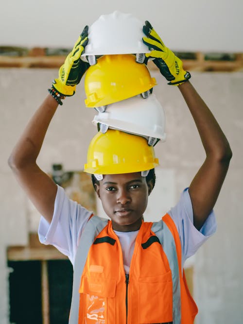 Free Woman Engineer Holding Stacked Hardhats on her Head  Stock Photo