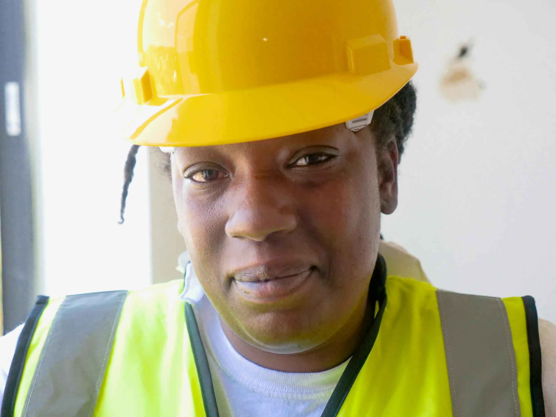Portrait of a female engineer wearing a yellow hardhat and safety vest indoors.
