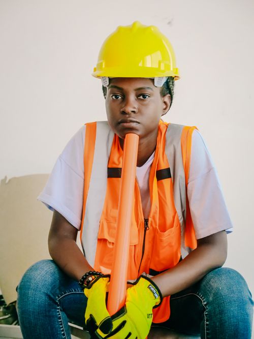 Free Young worker in construction gear with PPE sitting and holding a safety cone. Stock Photo