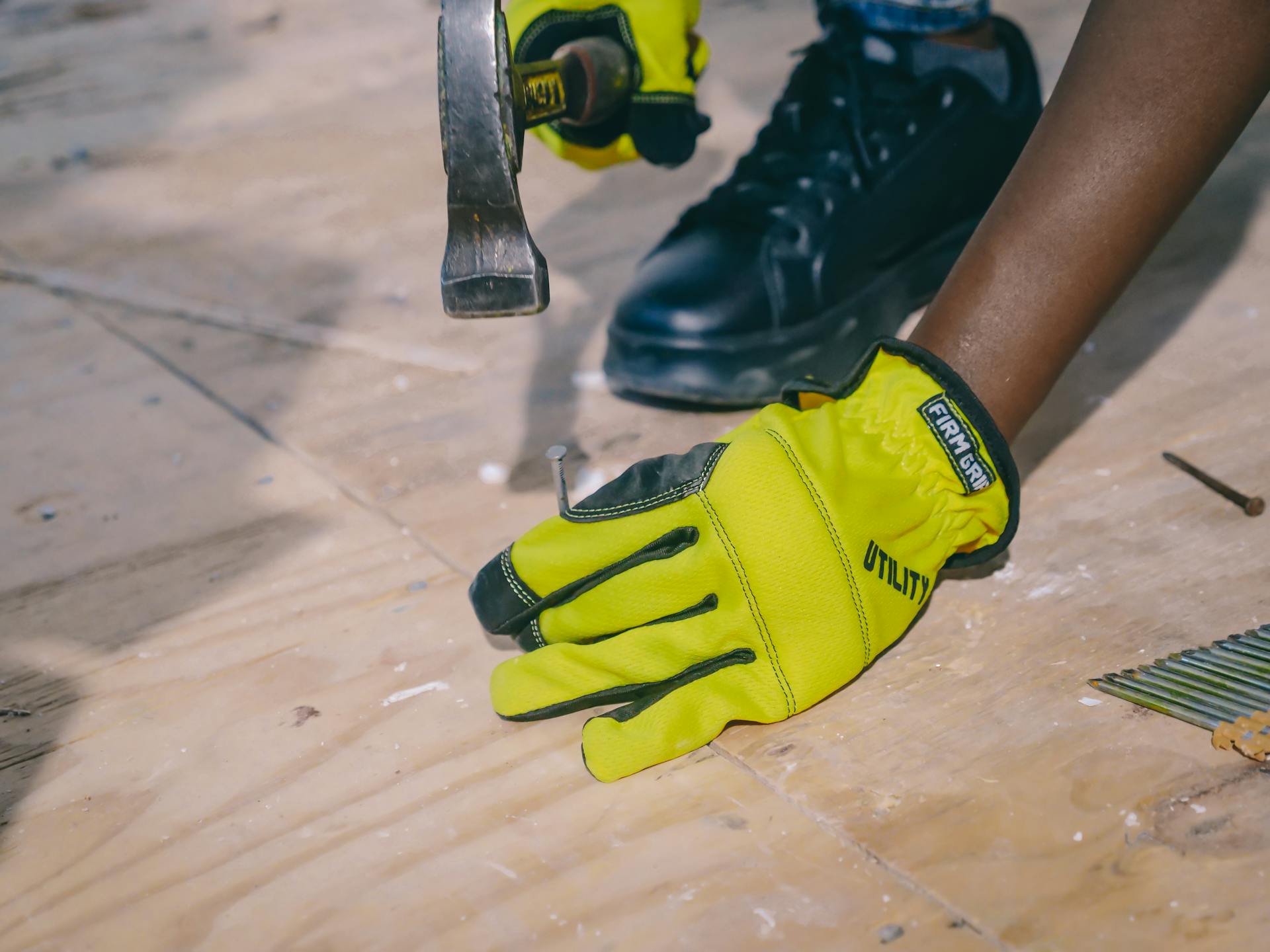 High angle view of a person wearing protective gloves and hammering nails into a wooden surface.