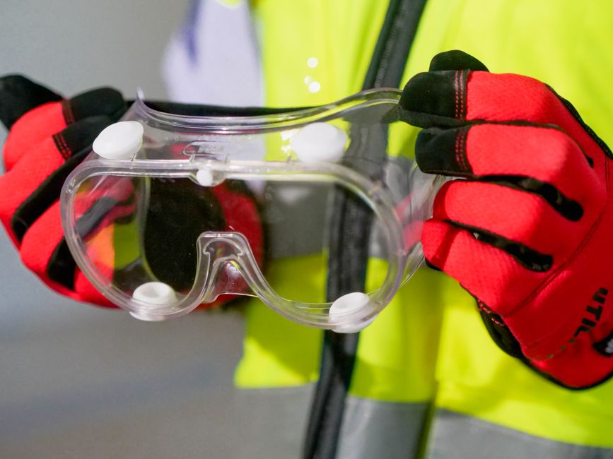 Imagen en primer plano de una persona sosteniendo gafas de seguridad con guantes protectores, enfatizando EPI.