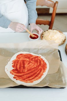 Homemade pizza dough topped with tomato sauce, ready for baking. Perfect for culinary enthusiasts.