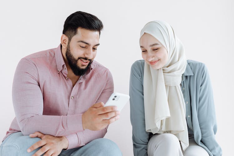 Bearded Man And Woman Wearing Hijab Looking At The Screen Of A Cellphone