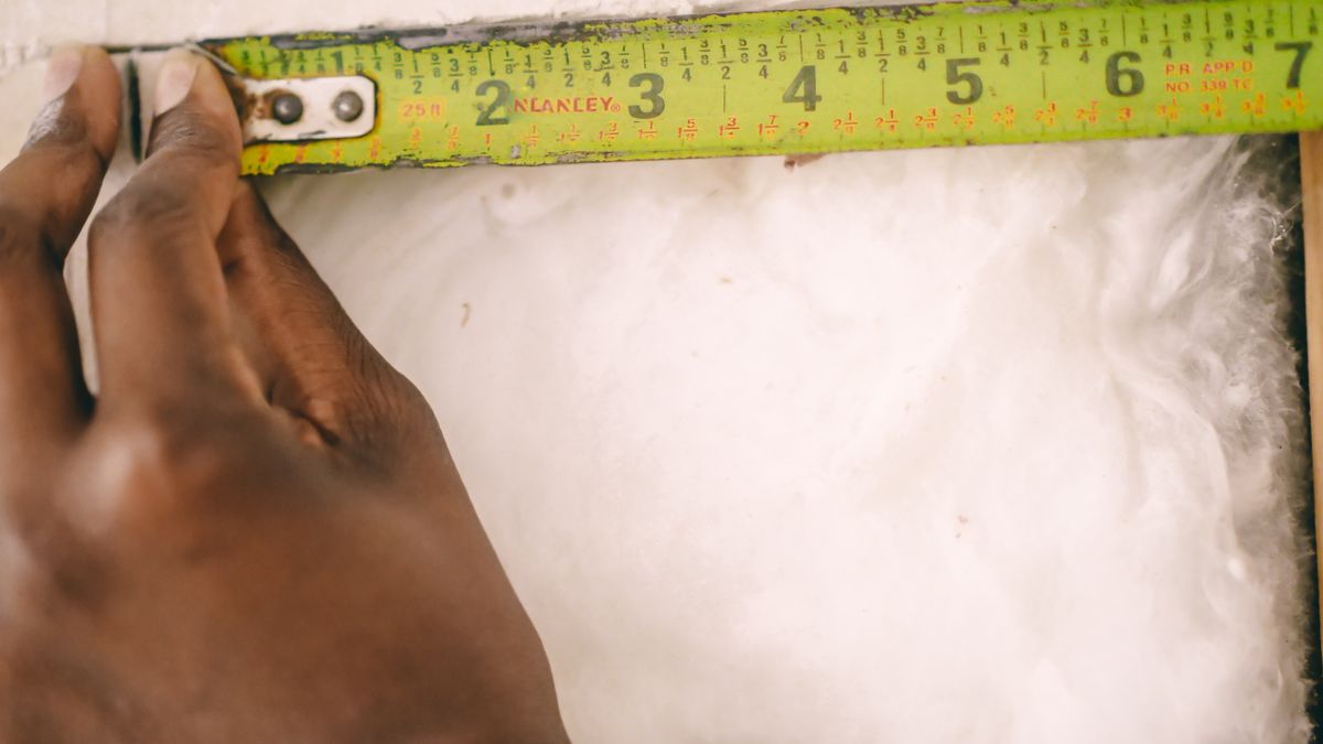 Measuring insulation thickness with a tape measure. Thickness is what sets the R-value of a batt.