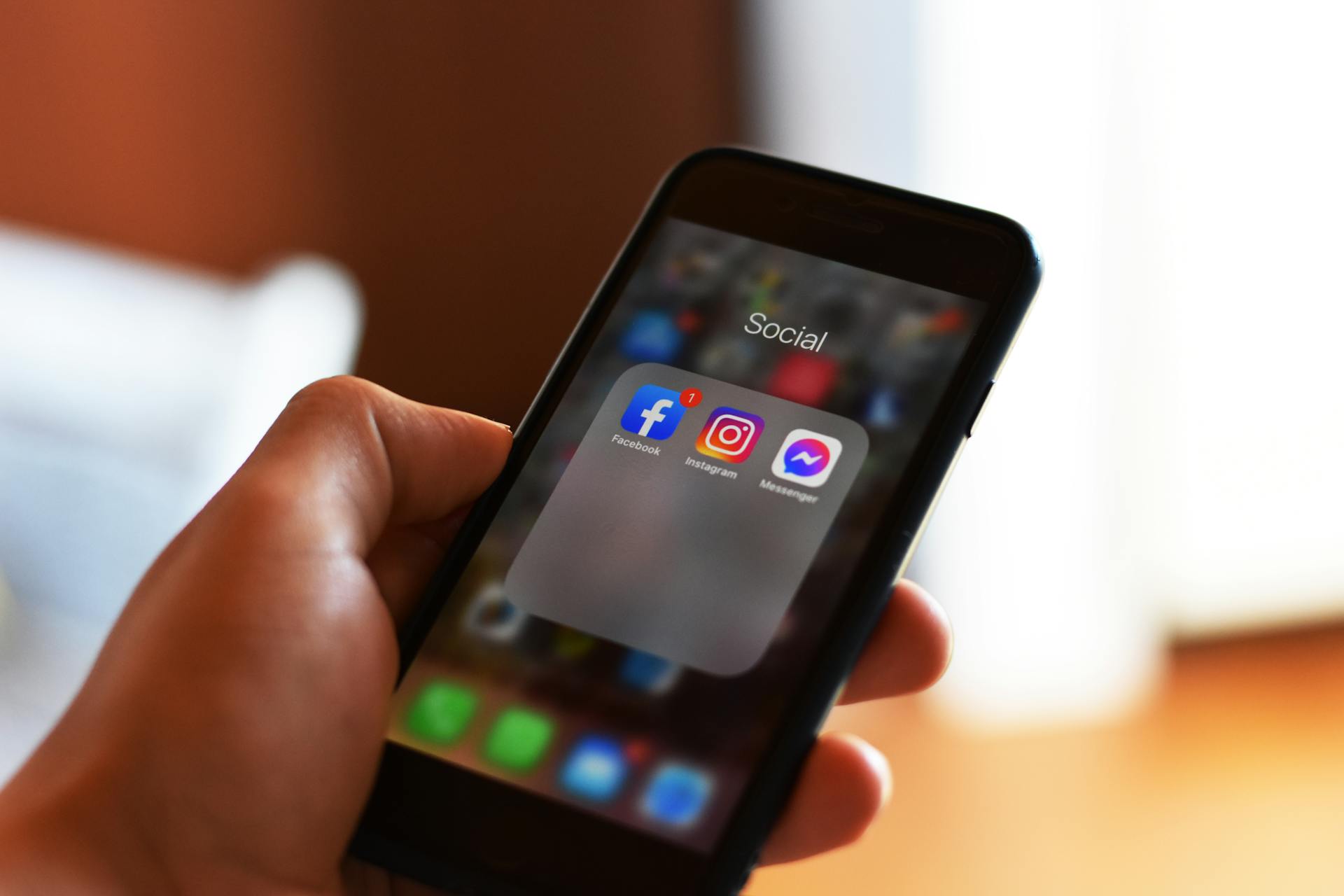 Close-up of hand holding smartphone showing social media apps like Facebook and Instagram.