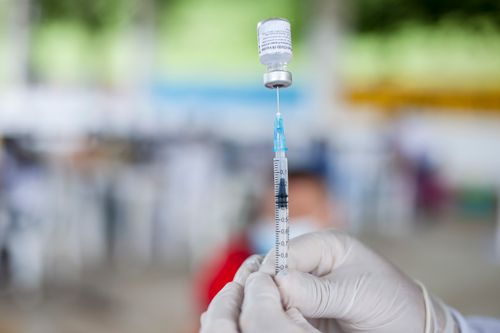 Free Close-up of syringe needle drawing COVID-19 vaccine from a vial held by gloved hands. Stock Photo