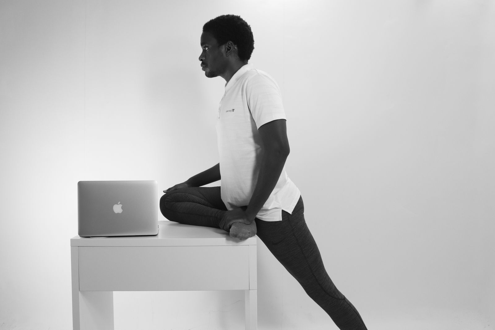 Man in a home office doing a leg stretch beside his laptop during a work break