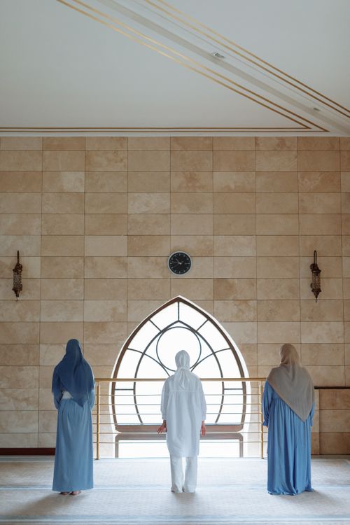 Free Three women in hijabs praying inside a mosque, facing a beautiful window during Ramadan. Stock Photo
