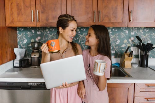 Mother and Daughter Smiling while Looking at Each Other Holding Mugs