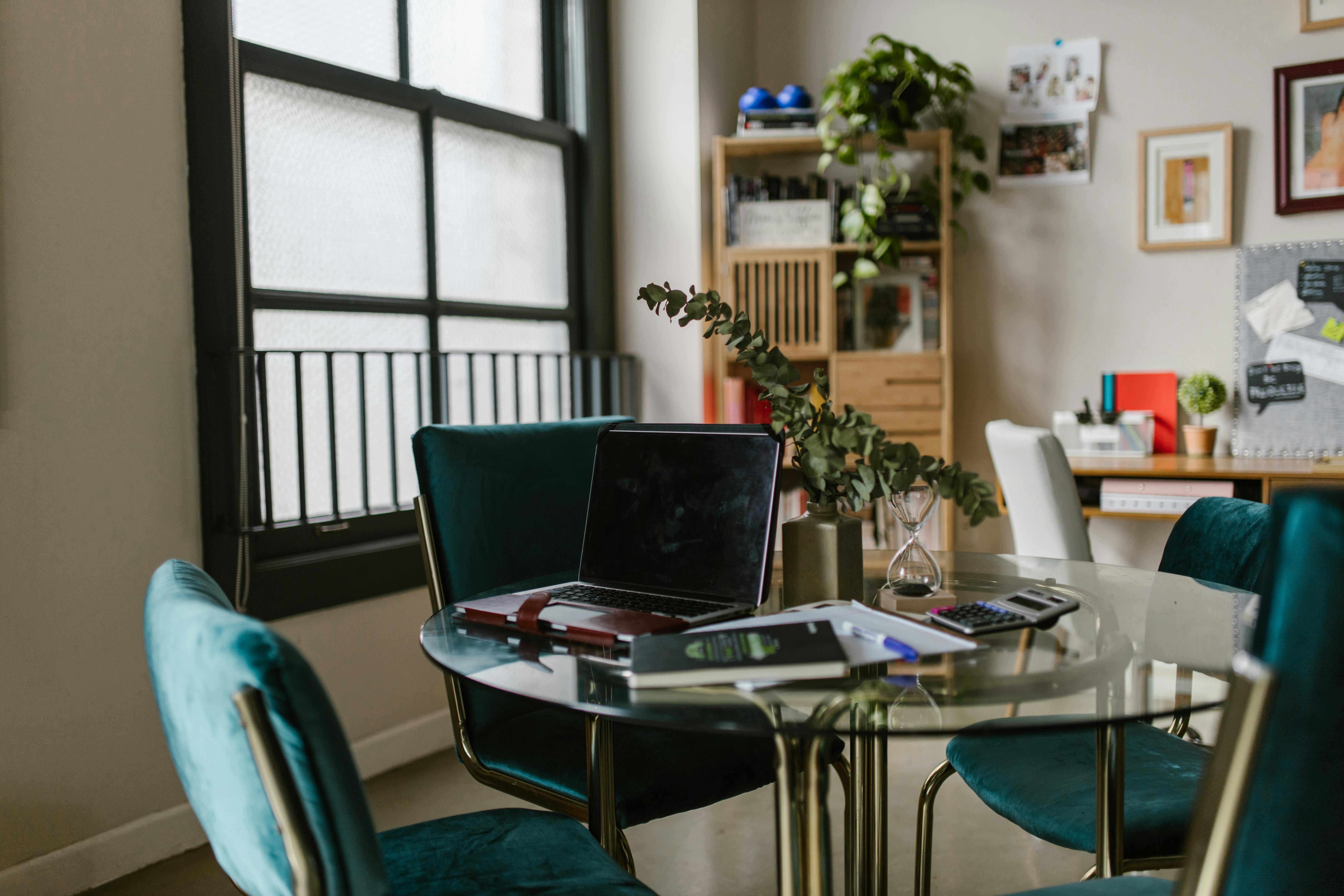 A contemporary home office featuring a glass table, laptop, and vibrant teal chairs, perfect for productivity.