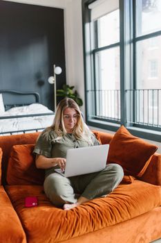 A woman comfortably seated on a sofa using a laptop in a cozy home setting.
