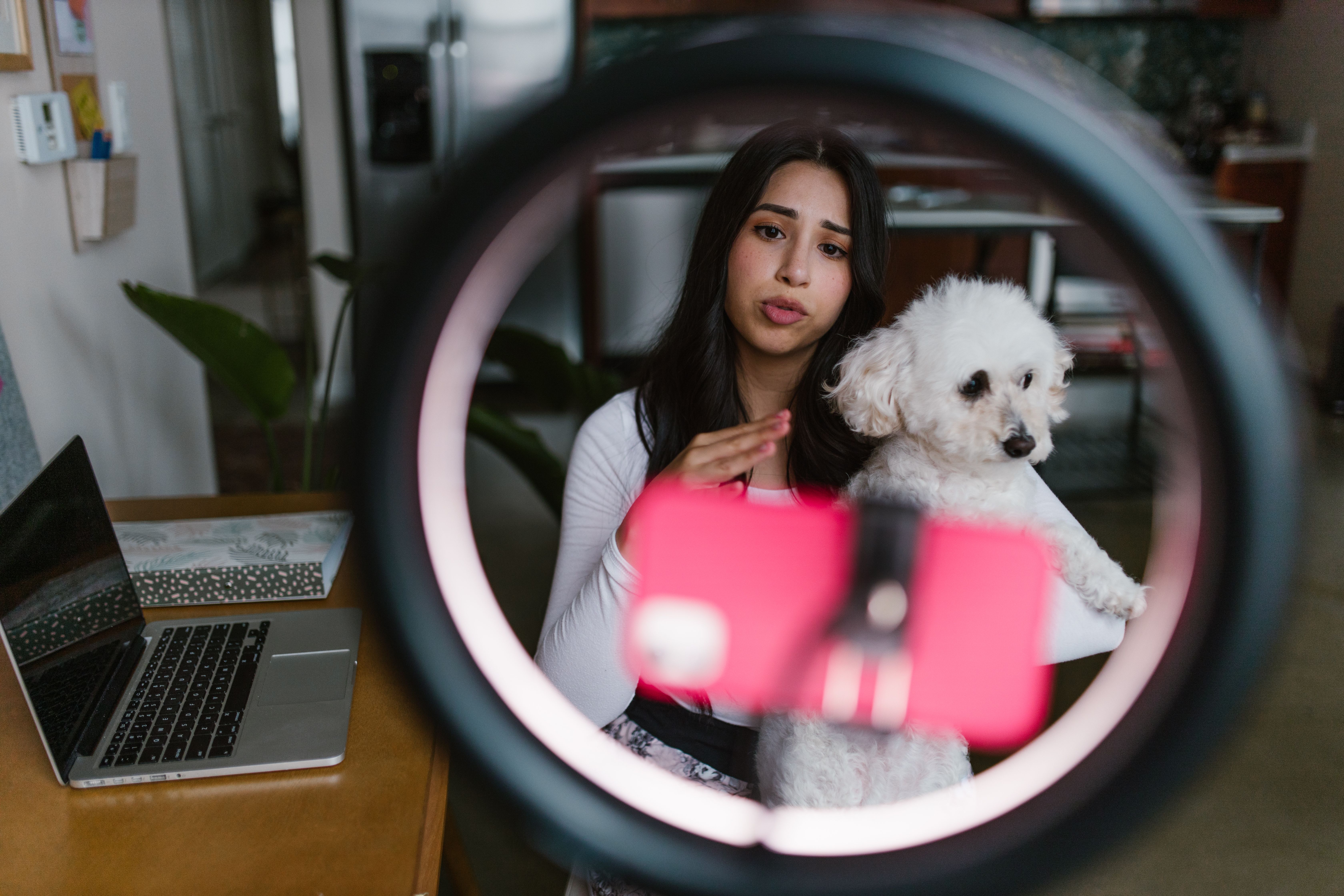 A person holding her dog in front of a phone attached to a ringlight