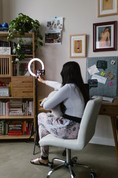 A woman and her dog posing for a selfie using a ring light in a cozy home office setting.