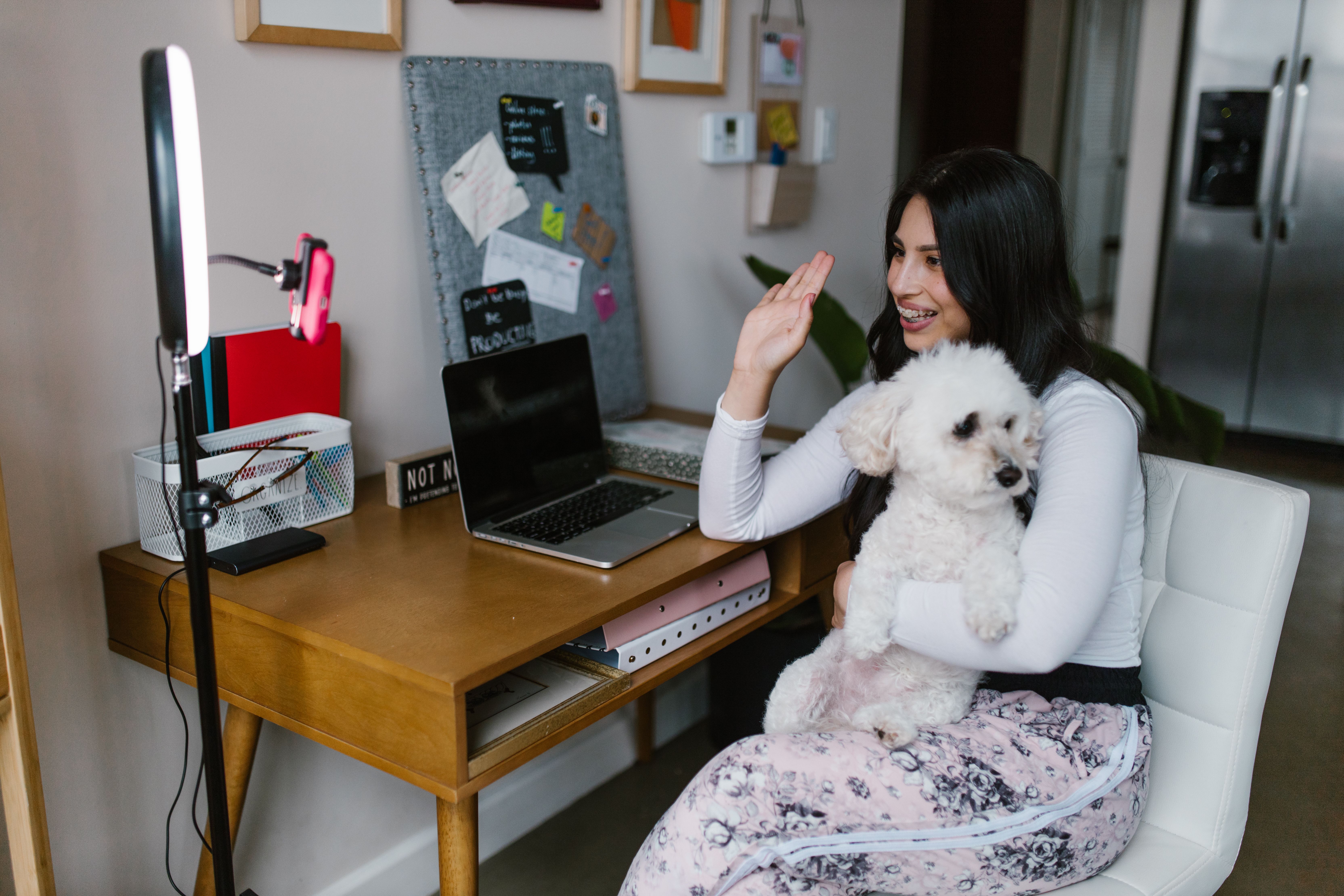 Young woman smiling at her desk with a dog, working from home in a cozy office setting.