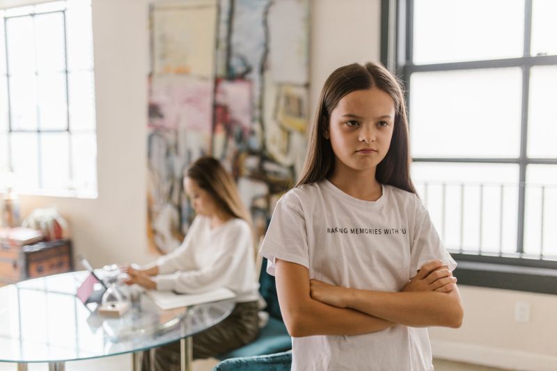 A defiant child standing with arms crossed as a parent looks on — the daily standoffs of Oppositional Defiant Disorder