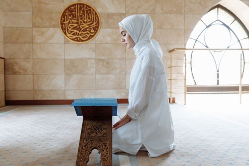 Free Muslim woman in traditional attire kneeling inside a mosque, engaging in prayer. Stock Photo