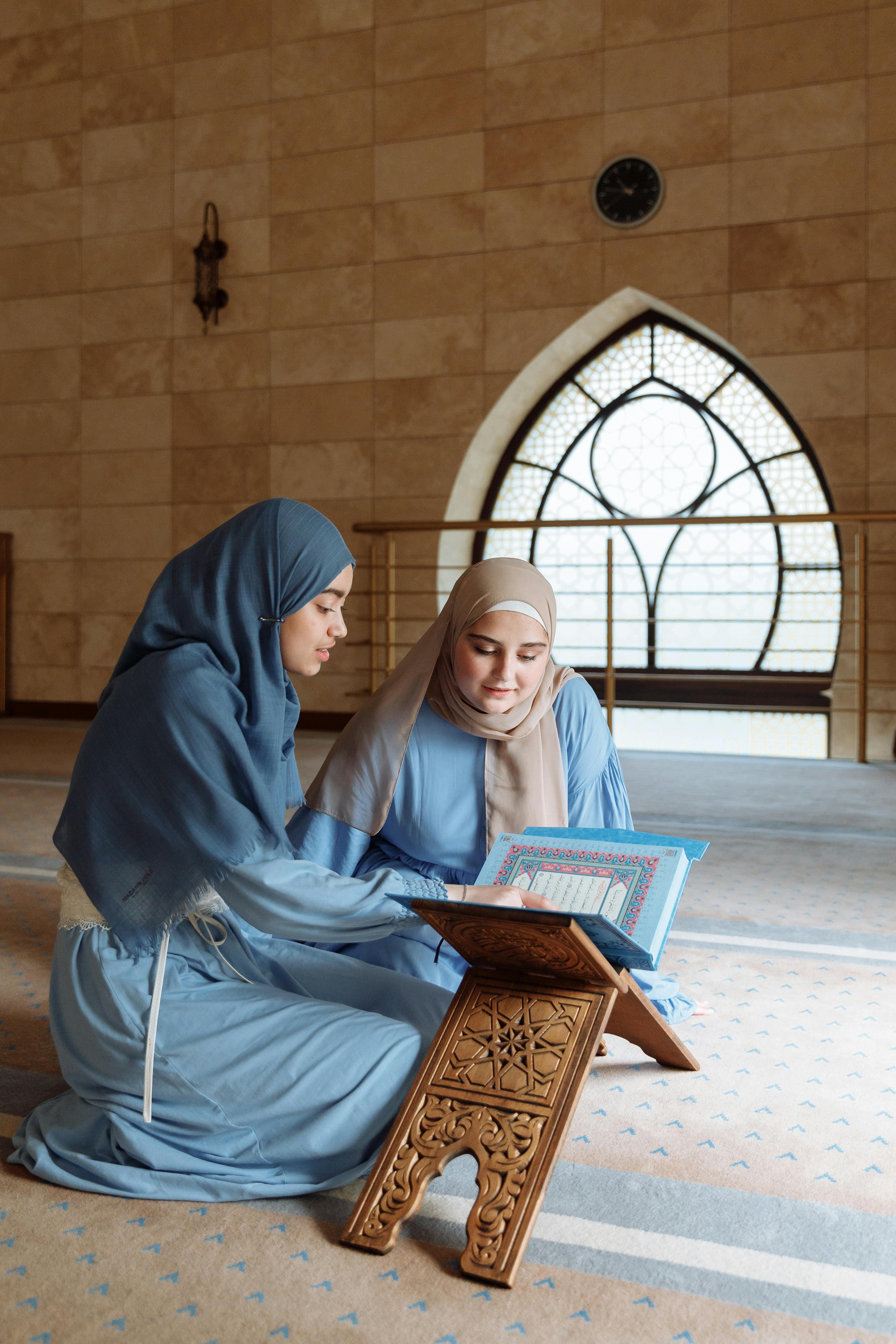 Two Muslim women in a mosque reading the Quran together, symbolizing faith and spirituality.