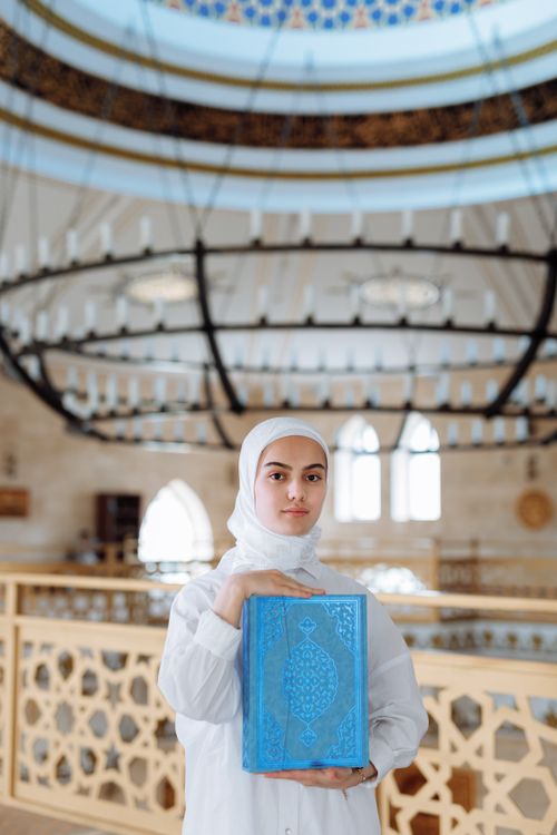 Free A woman in hijab holding the Quran inside a mosque, showcasing Islamic faith. Stock Photo
