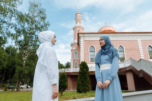 Free Two Muslim women in hijabs engage in conversation outside a mosque on a sunny day. Stock Photo
