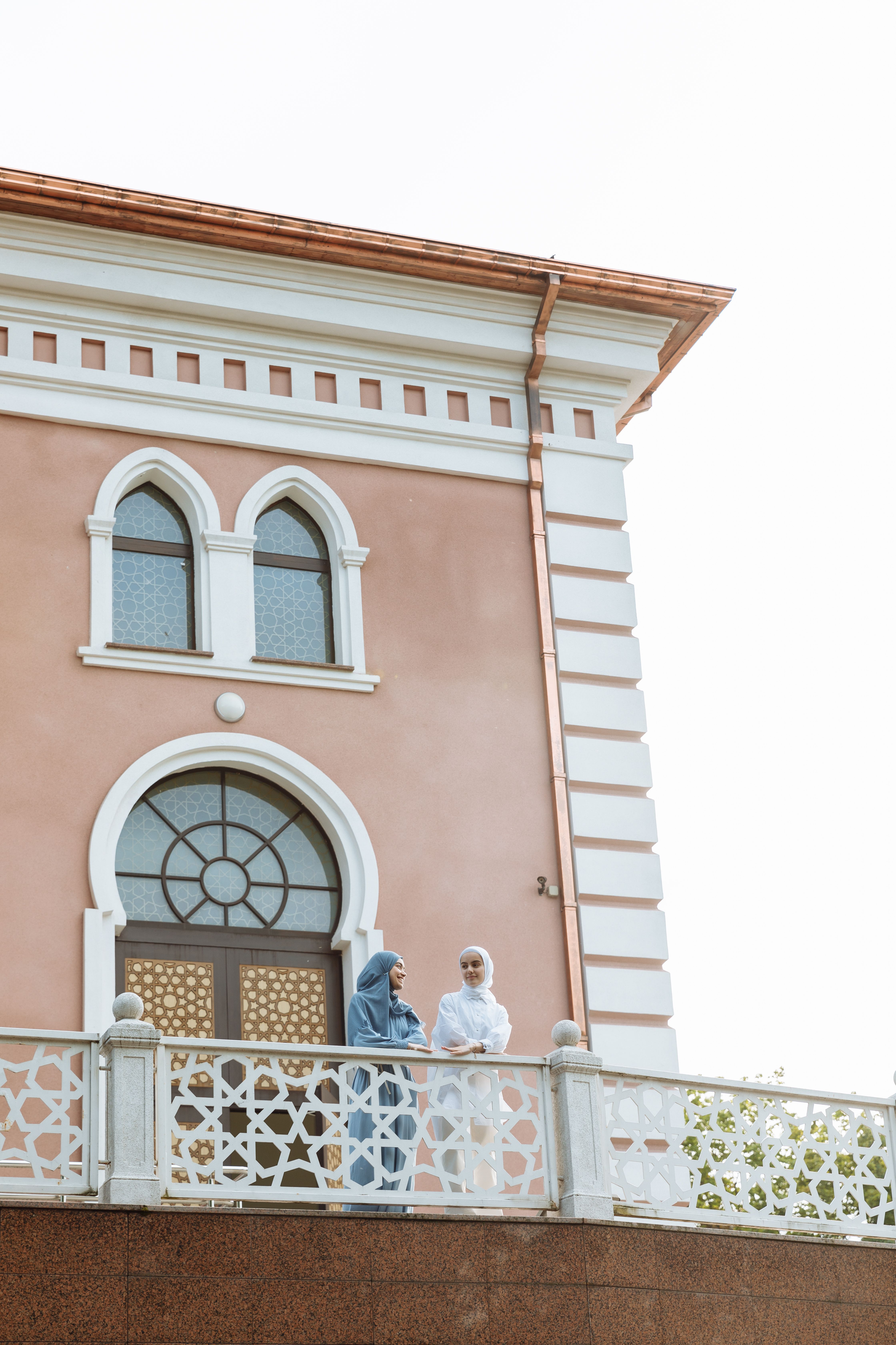 Two women in hijabs chatting on a balcony of a historic building.