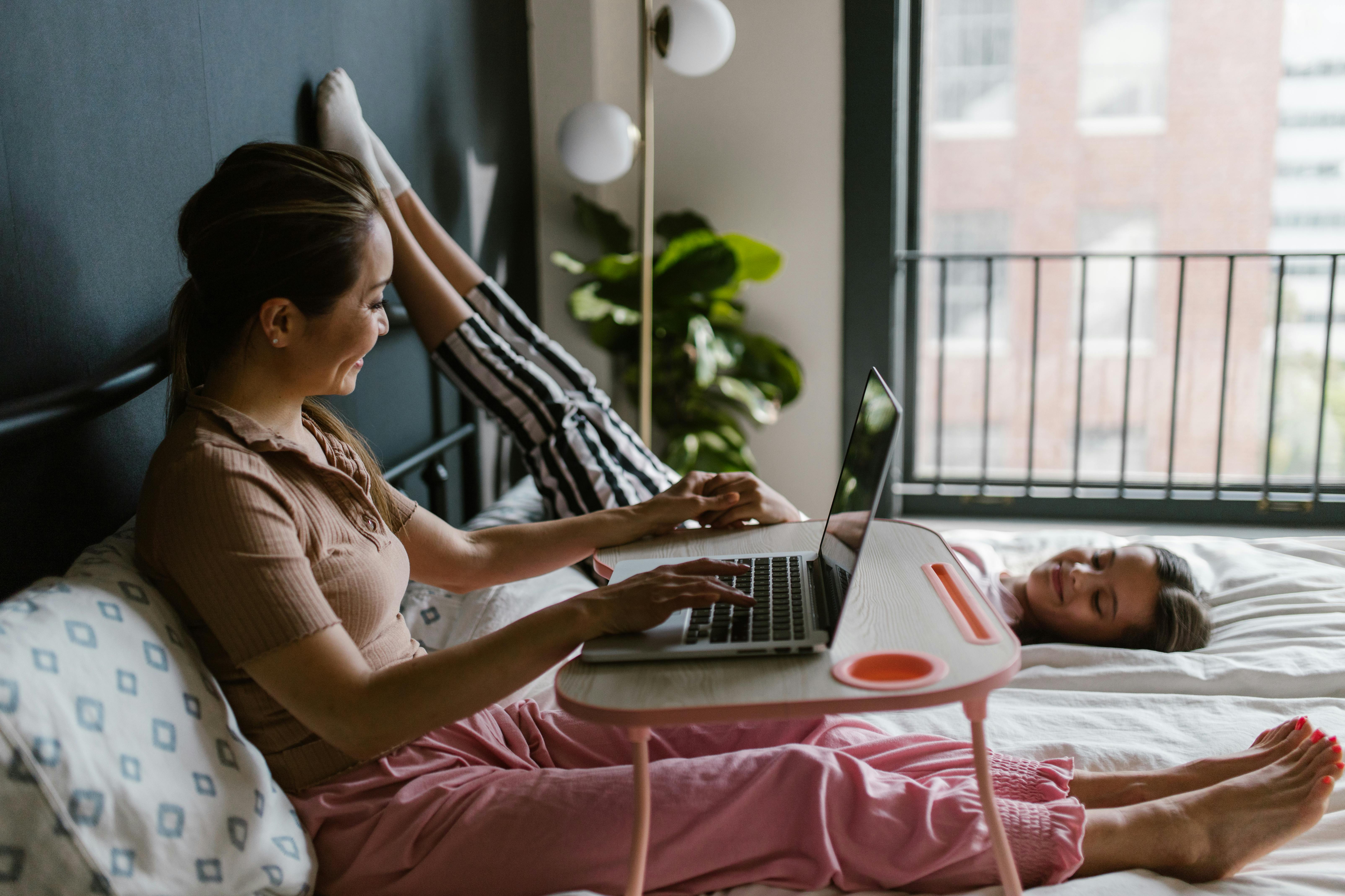 a woman with a child on bed while using a laptop