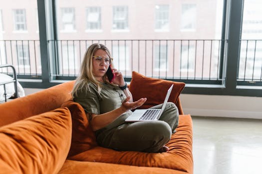 Woman working from home on a couch with a laptop and phone, showcasing remote work lifestyle.