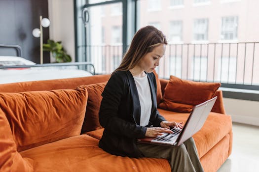 Woman working on a laptop in a modern living room with orange sofa.