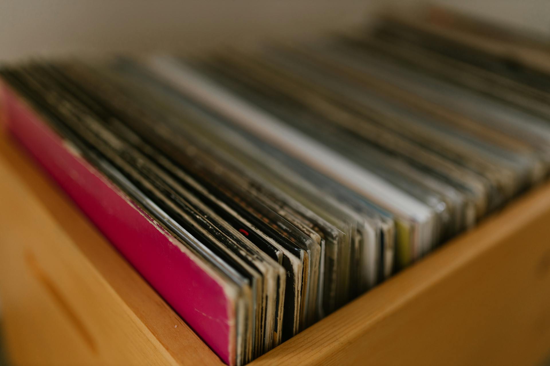 A collection of vintage vinyl records stored in a wooden shelf, showcasing a blurred background.