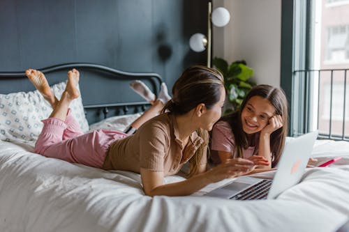 Mother and a Daughter Lying with a Laptop on a Bed