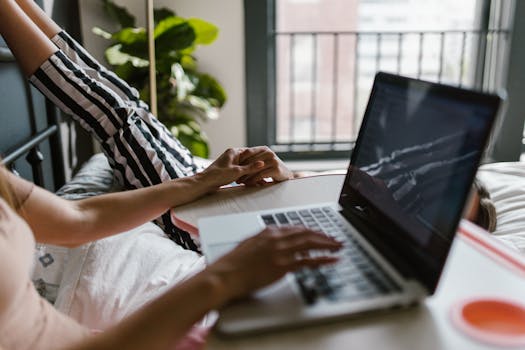 A mother and daughter holding hands while using a laptop at home, creating a supportive and loving atmosphere.