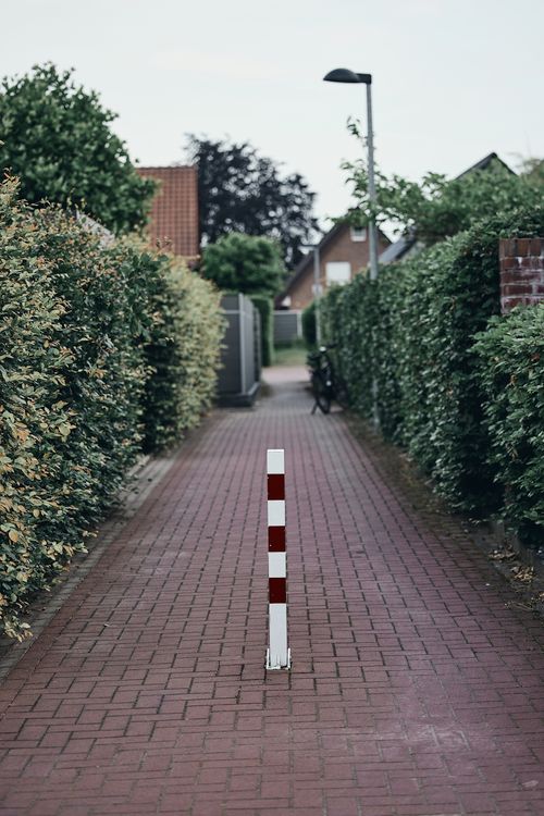 Free Brick pathway lined with hedges, featuring a red and white bollard in a residential area. Stock Photo