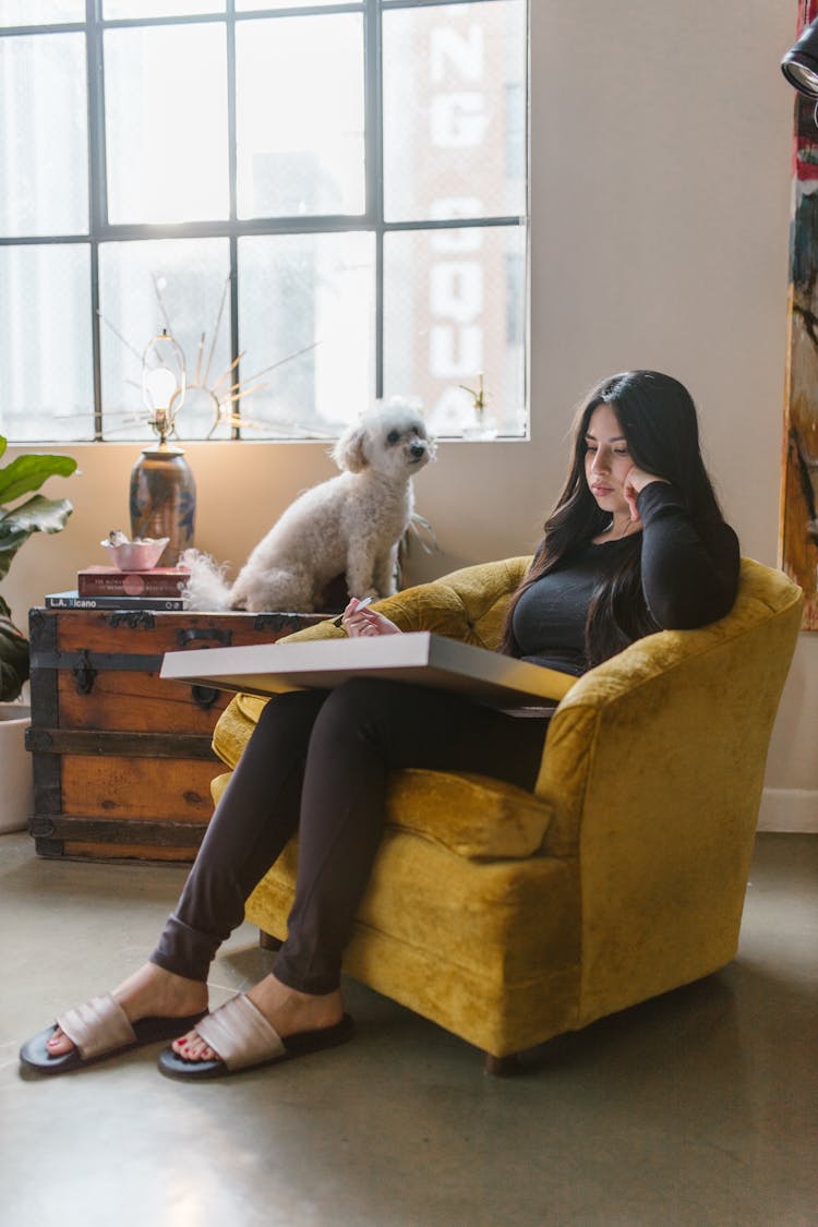 A Woman In Black Long Sleeves Sitting On The Chair Near Her Dog