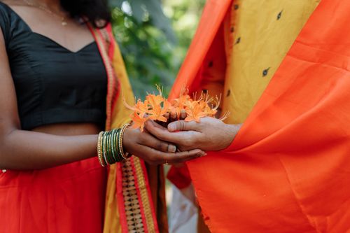 Free Close-up of a traditional Indian ceremony with a couple holding vibrant orange flowers. Stock Photo
