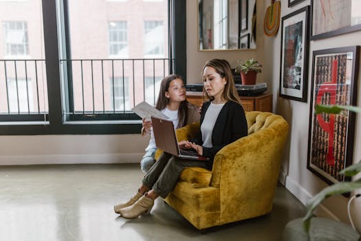 Mother and daughter together during remote work at home, balancing parenting and productivity.