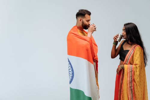 Free A man and woman in traditional attire drinking while wrapped in the Indian flag indoors. Stock Photo