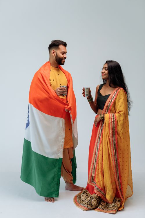 Free A couple in traditional Indian attire, wrapped in the Indian flag, share a joyful moment holding cups. Stock Photo