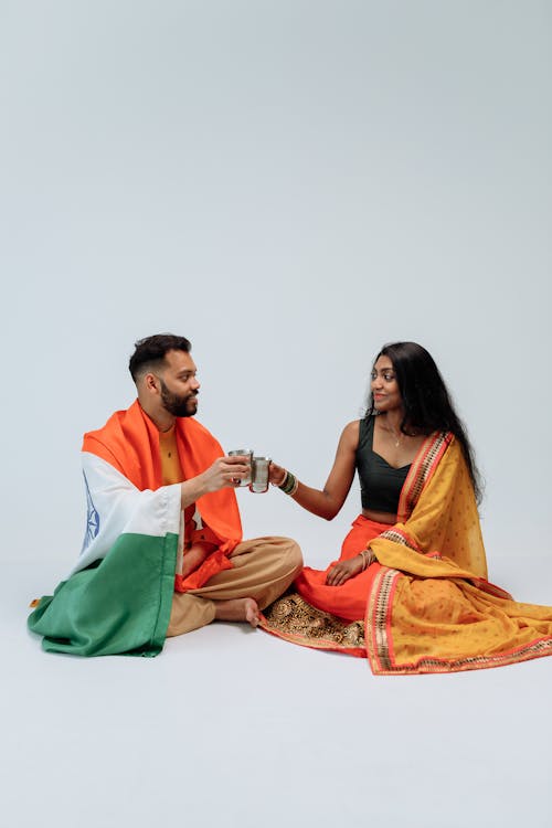 A Man and a Woman in Traditional Outfit Sitting on the Floor while Having a Toast