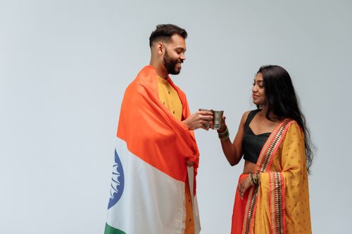 Free Two South Asian adults toasting with steel cups in traditional attire, wrapped in the Indian flag. Stock Photo